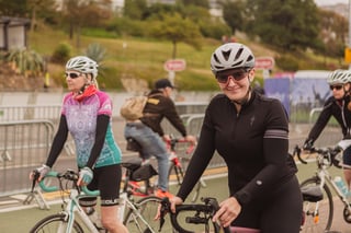 A smiling rider in a black jersey and pink-rimmed glasses rolls past barriers at the Women's Tour of Britain finish.