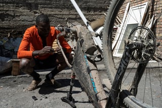 Rider crouches in a Talas yard repairing a muddy bike with its front wheel off during the Silk Road Mountain Race.