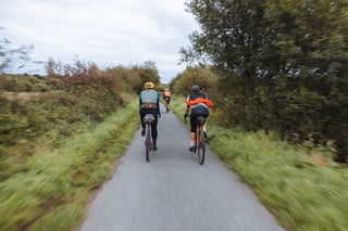 Three riders on gravel bikes follow a narrow tarmac cycle path between hedges on the Isle of Wight.
