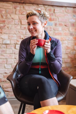 A smiling rider in a purple jacket cradles a red coffee cup in a brick-walled café on the Isle of Wight.