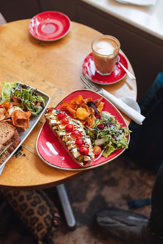 Open sandwich, salad and a latte on a small café table during the Isle of Wight glampacking weekend.
