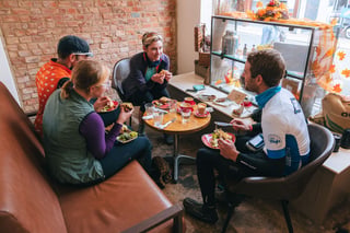 Four riders share lunch and coffee around a small table in a café on the Isle of Wight, autumn leaves in the window.