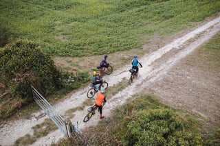 Drone view of four riders on bikepacking-style gravel bikes heading along a chalky farm track past a gate.