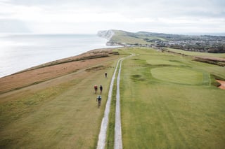 Aerial view of riders on a chalk double track beside a clifftop golf course on the Isle of Wight, white cliffs beyond.