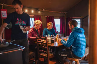 Riders sit down to breakfast inside the safari tent at Tapnell Farm while another cooks at the stove.