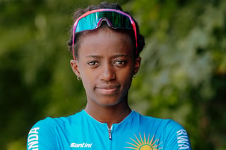Jazilla Mwamikazi in Rwanda national kit and mirrored sunglasses, looking at the camera in front of green trees.