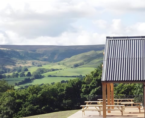 Covered picnic benches at the Yorkshire Cycle Hub, overlooking green moorland hills in Great Fryup Dale.