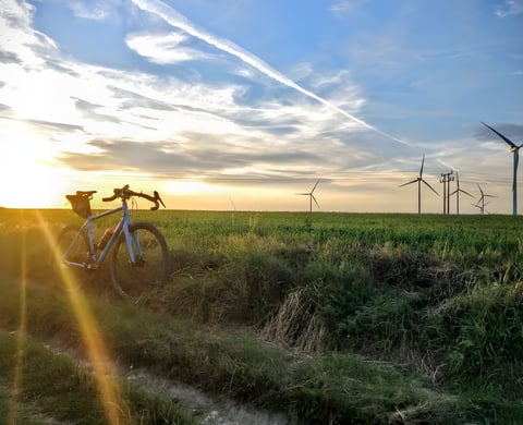 Gravel bike with a saddle pack leans in a grassy field at sunset, wind turbines on the horizon, for the Peddars Way route.
