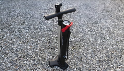 Bontrager Flash Charger tubeless track pump standing on gravel, with red charge lever and pressure gauge.