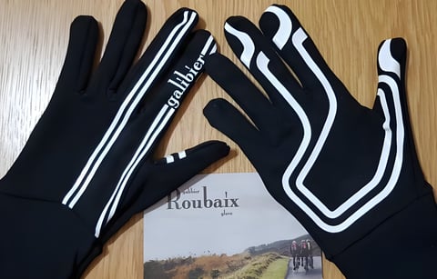Pair of black Galibier Roubaix Vision gloves with white stripes lying on a wooden table beside a Roubaix glove leaflet.