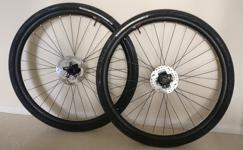 Homebrew carbon gravel wheelset with Panaracer GravelKing SK tyres and Shimano disc rotors, leaning against a wall.