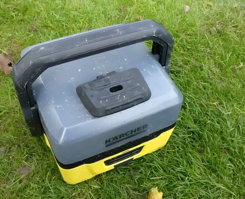 Kärcher OC3 portable washer with grey water container and yellow base standing on grass.