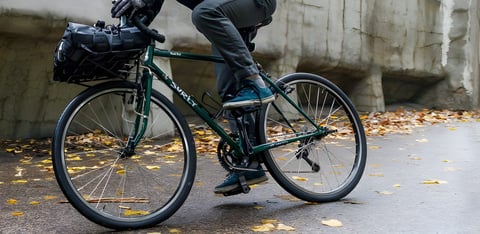 Surly Pack Rat randonneur bike in green with a front bag on a porteur rack, ridden over autumn leaves.