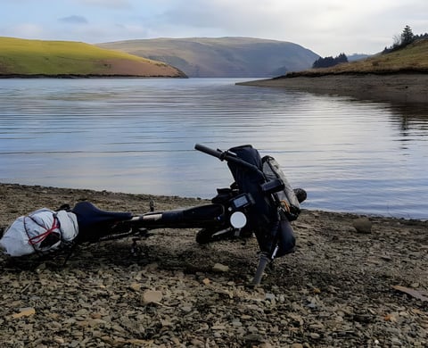 Loaded bikepacking bike lying on the shingle shore of Clywedog Reservoir during the Bearbones Café Racer ride in Mid-Wales.