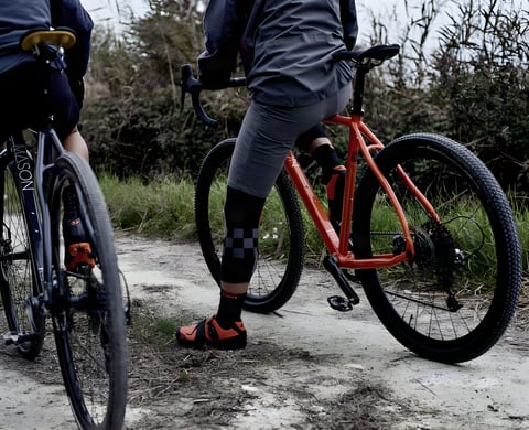 Two riders pause on a chalky track, one astride an orange Mason Bokeh adventure bike, the other on a dark one.