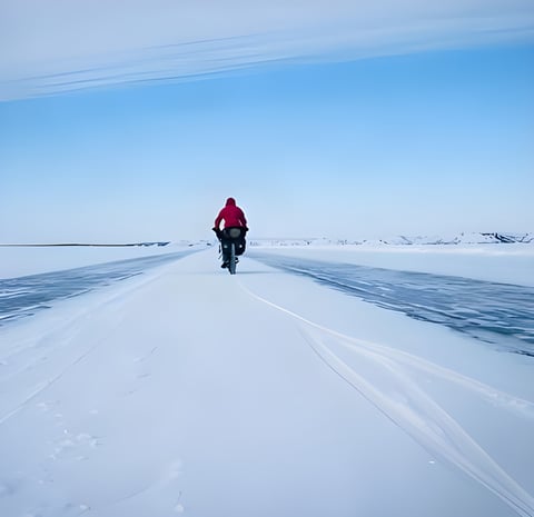 Cyclist in a red jacket rides a loaded fatbike across snow and ice, a still from The Frozen Road film in Canada's Yukon.
