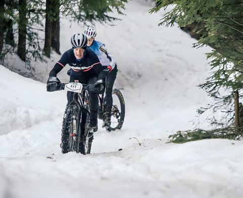 Two fatbike riders descend a snowy forest track on Stage 3 of the Snow Bike Festival in Gstaad.