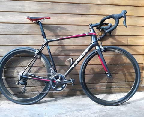 Trek Emonda SL road bike in charcoal and red with Shimano Ultegra and deep carbon wheels, against a timber wall.