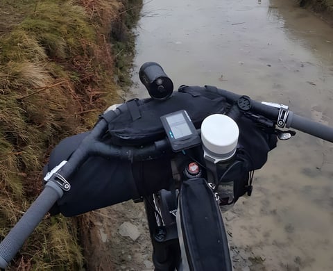 Wahoo ELEMNT GPS bike computer on the handlebars of a loaded bike, above a flooded track.