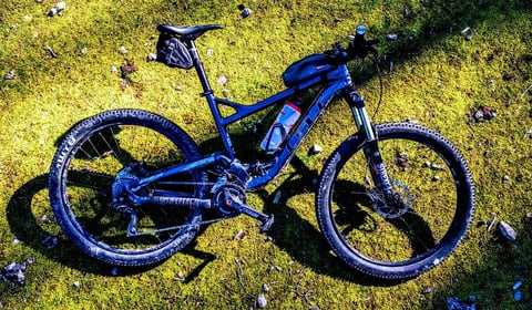 GT full-suspension mountain bike with saddle bag and top-tube bag lying on mossy ground on the Mallorca tour.