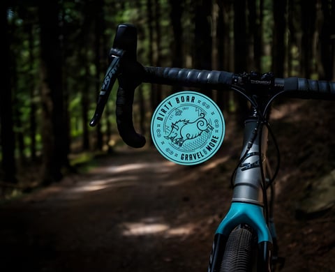 Dirty Boar Gravel Ride logo over the drop bars of a gravel bike on a shaded forest track.