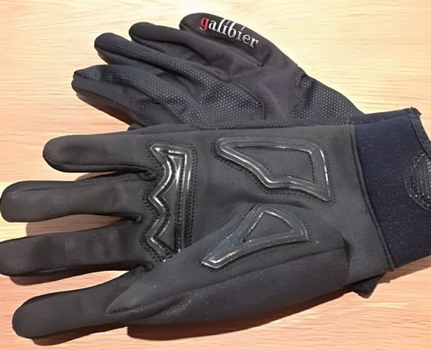 Pair of black Galibier Ardennes winter gloves with silicone grip detailing on the palm, on a wooden table.