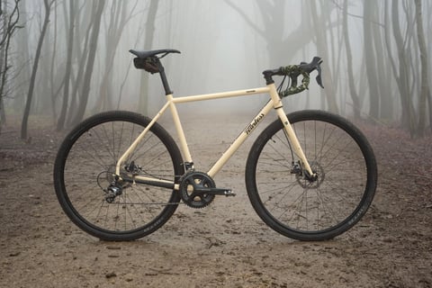 Cream Fearless Vulture steel gravel bike with Shimano Ultegra cranks, stood in a misty woodland clearing.
