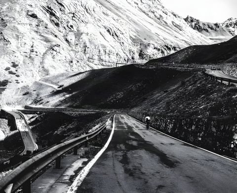 Lone rider climbs a winding Alpine pass road on the Transalp ride from Germany to Italy, in black and white.