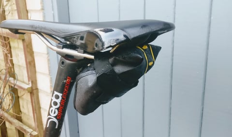Apidura Expedition Tool Pack from behind, its yellow light attachment point visible below the saddle.