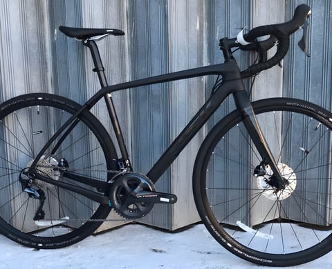 Matt black Trek Checkpoint gravel bike with Shimano Ultegra cranks and Schwalbe tyres, leaning on a metal wall.