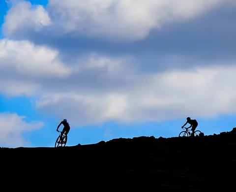 Two Dirty Reiver riders silhouetted against a cloudy blue sky on a hilltop in Kielder, Northumberland.