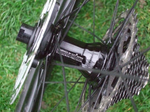 Hunt 30 Carbon Gravel rear hub on grass, its Bearings by EZO Japan label between the cassette and rotor.