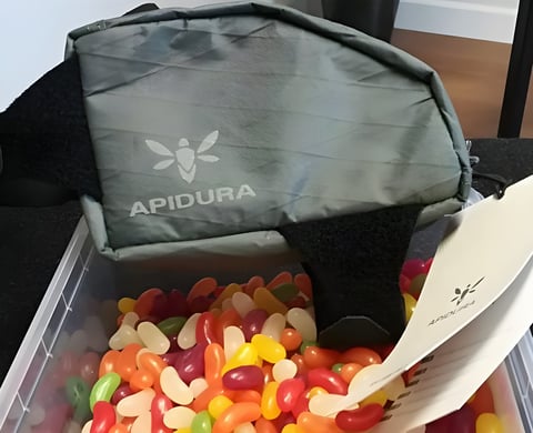 Apidura Backcountry Top Tube Bag 0.5L sitting on a tub of jelly beans, with its product tag beside it.