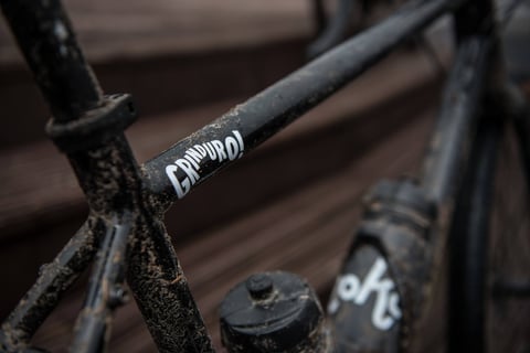 Close-up of a Grinduro sticker on the muddy top tube of a gravel bike.