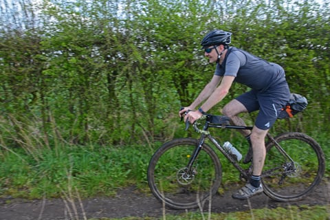 Rider in grey kit on a Fearless Vulture gravel bike along a muddy hedge-lined track in the Chilterns.