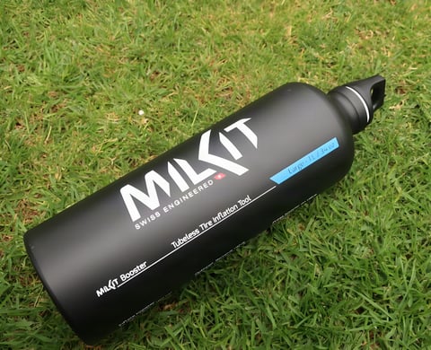 MilKit Booster tubeless inflator's black 1 litre aluminium bottle lying on grass.