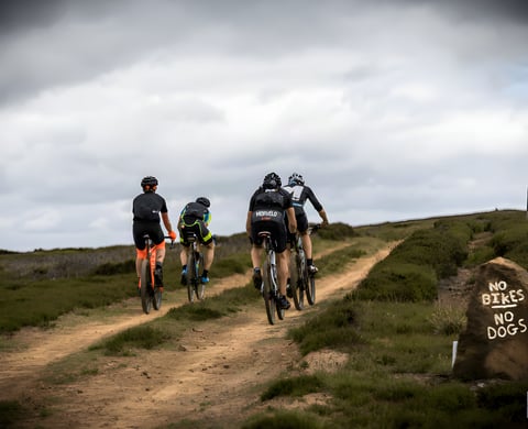 Riders on a moorland track at Yorkshire True Grit with a hand-painted No Bikes No Dogs sign on a rock.