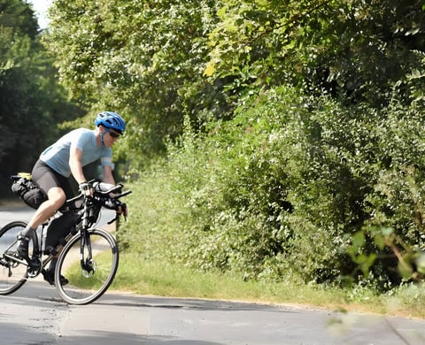 Rider on a loaded Kinesis GTD titanium ultra-endurance bike with frame and saddle bags on a leafy lane.