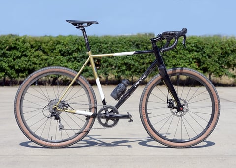 Jordan Lunn's gold and black All-City Cosmic Stallion gravel bike with tan-wall WTB tyres, side on in the sun.