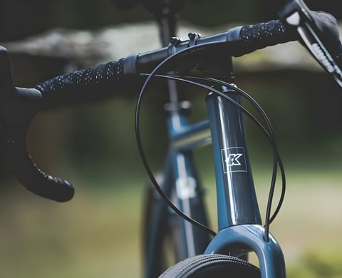 Close-up of the Kinesis G2 gravel bike's blue head tube, Kinesis badge, bar tape and external cables.