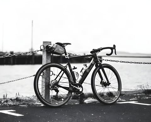 3T Exploro ridden at Grinduro Scotland, in black and white, with a saddle bag, leaning on a chained post by the docks.