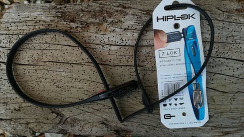 Hiplok Z Lok zip-tie lock in black laid on a weathered log next to its retail card.