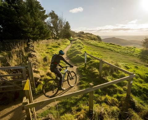 Top of the Rock rider passes a gate on a hillside trail above the North Yorkshire countryside, another rider ahead.