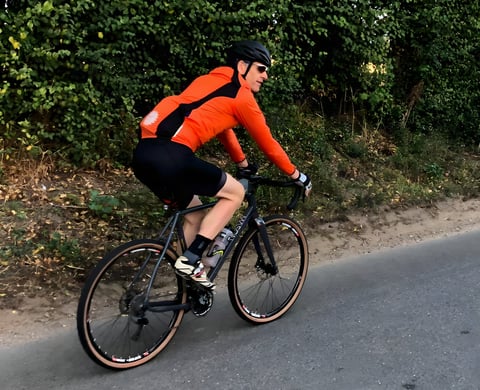 A cyclist in an orange Galibier VentUltra jacket rides along a country lane.