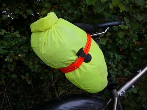 Orange Voile strap pulled tight around a hi-vis yellow dry bag mounted under the saddle of a mudguarded bike.