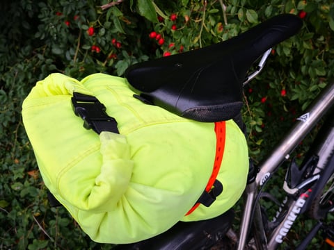 Top view of a rolled hi-vis dry bag seat pack held beneath the saddle by a single orange Voile strap.
