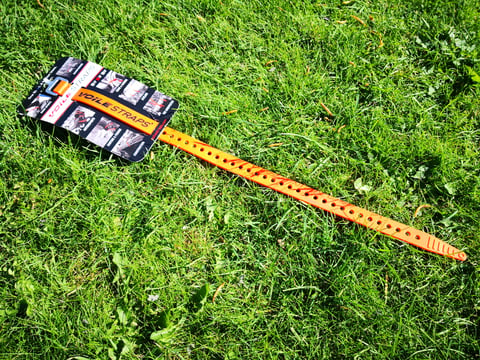 Full-length orange Voile Strap with its row of adjustment holes laid out on grass beside its retail card.
