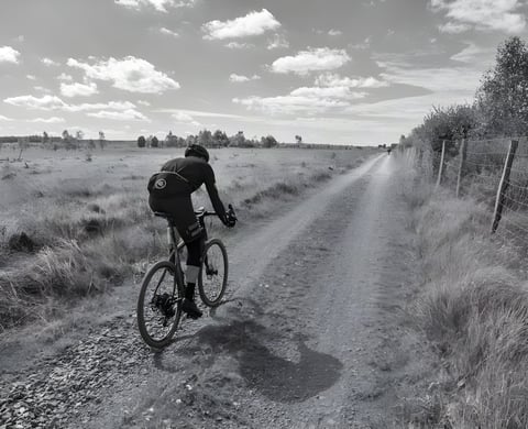 Rider on a gravel bike on a fenced heathland track at the Dirty Boar in Belgium, in black and white.