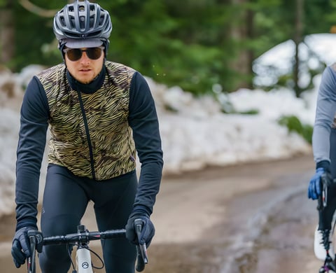Rider on a snowy road wearing the Café du Cycliste Heidi Luxe jacket in camaieu pattern, another rider alongside.