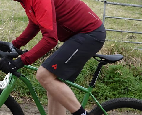 Aussie Grit Apparel Ignite 2-in-1 bib shorts on a rider pedalling a green gravel bike, reflective leg stripe showing.